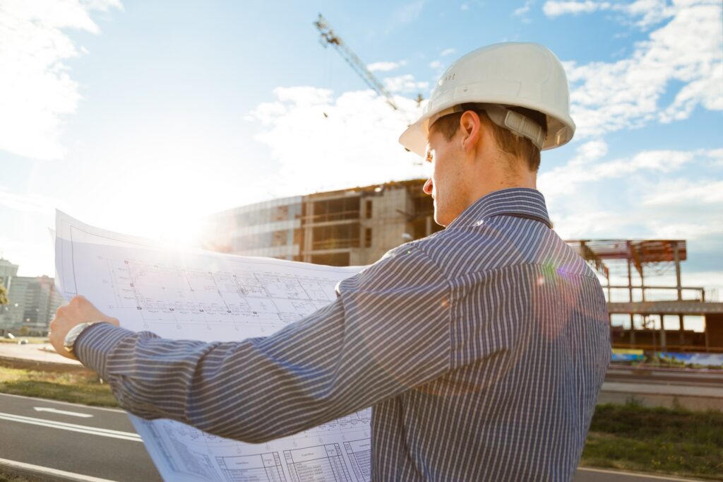 Architect in helmet with blueprints looks at camera in a building site